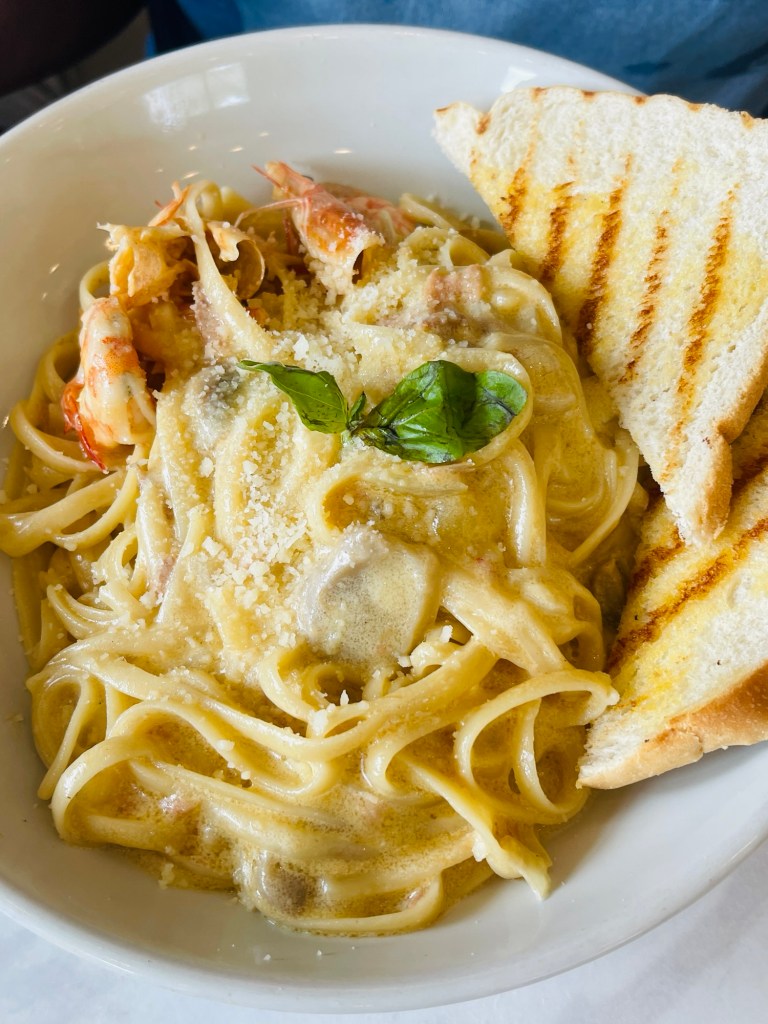A plate of Creamy Shrimp and Tuna Pasta topped with shrimps, garnished with a basil leaf, served with two slices of grilled bread.