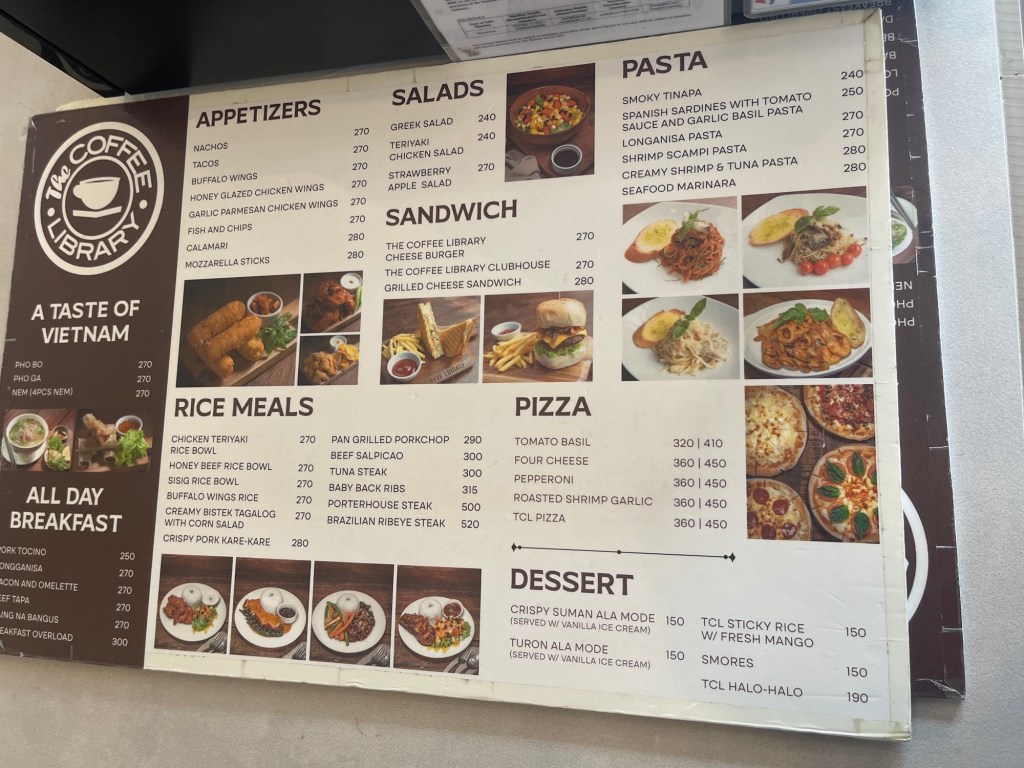 Menu board displaying various food options at The Coffee Library, including appetizers, salads, pasta, sandwiches, rice meals, pizza, and desserts, along with their prices.
