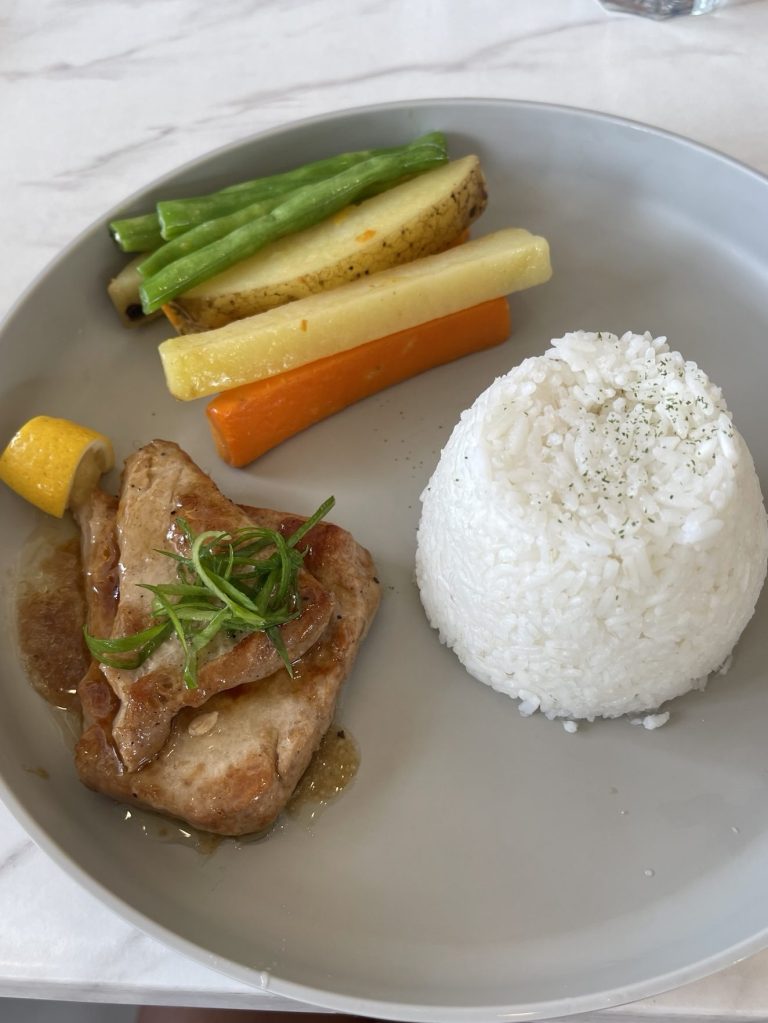 A plated meal featuring a grilled tuna steak garnished with green onions, accompanied by a serving of white rice and colorful vegetables including green beans, potato and carrot.
