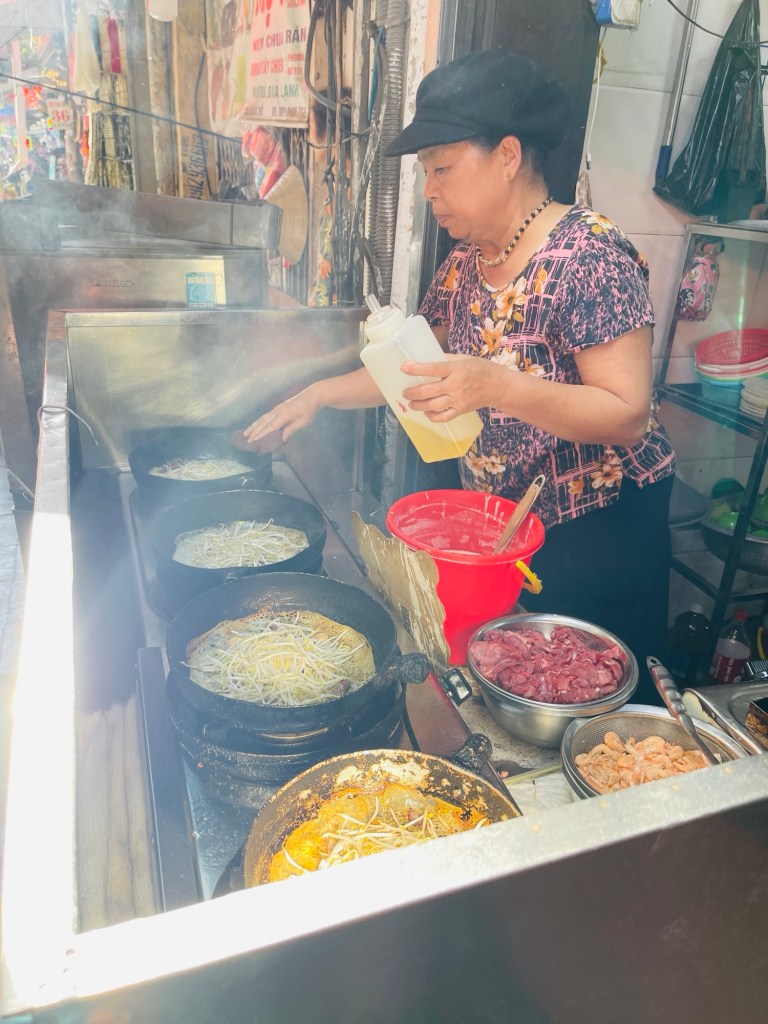 Lady cooking Banh Xeo on several pans​
